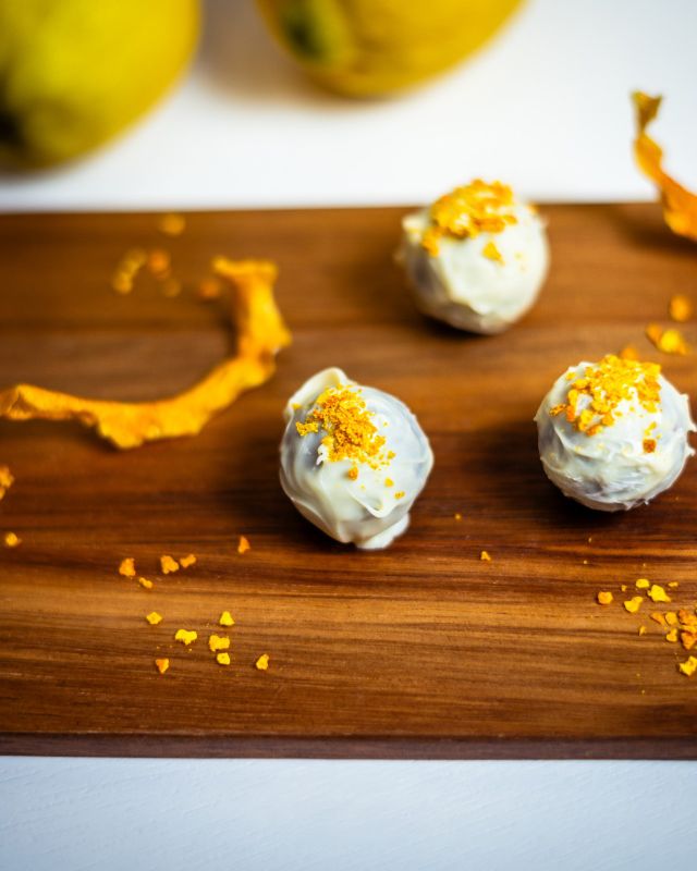 Trufas Lemon Gold cobertas de chocolate branco e raspas douradas, com limões ao fundo